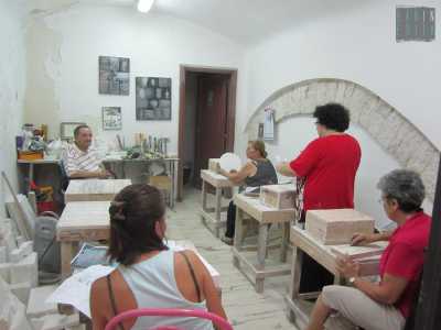 Quando andiamo a parlare con Antonio lo troviamo con quattro signore intente a lavorare la pietra con scalpello e martello su piccoli tavolacci in legno, in un ambiente pregno di polvere